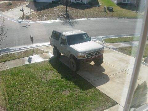 1995 Ford Bronco - A lifted Ford Bronco sits in a suburban driveway on a cloudy day.