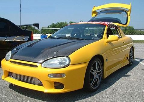 1994 Ford Probe - A bright yellow sports car with a carbon fiber hood and a prominent rear spoiler is parked with its hatch open.