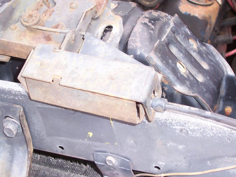 Close-up of a rusty metal bracket and cable assembly, possibly from an engine bay
