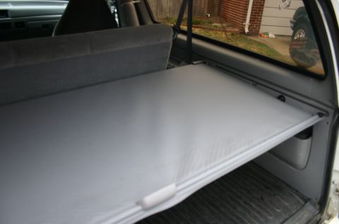 1994 Ford Bronco - gray retractable cargo cover pulled out over the rear cargo area of an SUV, viewed through the open hatch.