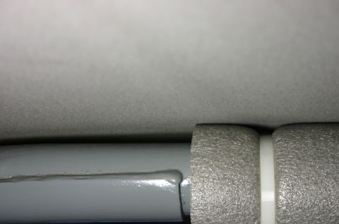 1994 Ford Bronco - Tight macro detail of grey interior trim: a fuzzy grey headliner-style fabric surface above, a freshly painted glossy grey tube or bar runn…