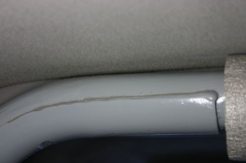1994 Ford Bronco - Extreme close-up of a freshly painted light grey interior roll bar or windshield-header tube meeting grey headliner fabric, with a visible…
