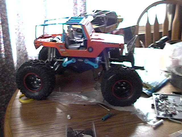 RC rock crawler with orange body and large tires on a wooden table