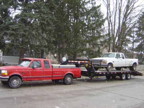 1992 Ford Bronco - Red Ford pickup tows a white Ford pickup on a trailer. The white truck is likely a 1992 model.