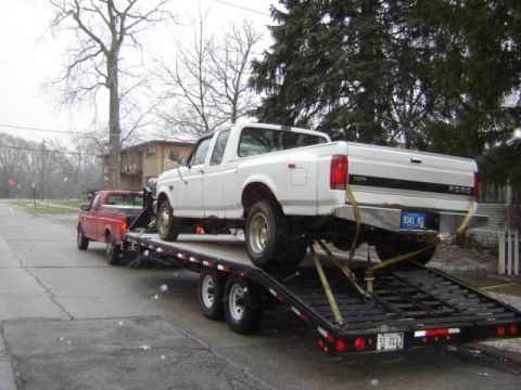 1992 Ford Bronco - A white Ford F-350 dually pickup truck is being transported on a trailer, with a red pickup truck towing it.