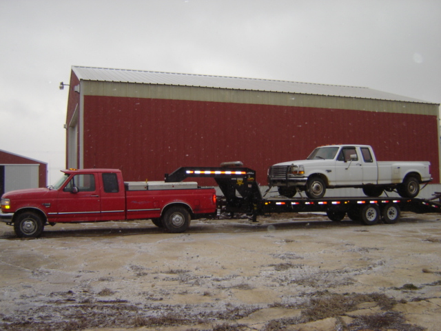 Side view of a red 1992 Ford F-250 towing a trailer carrying a white 1992 Ford F-350