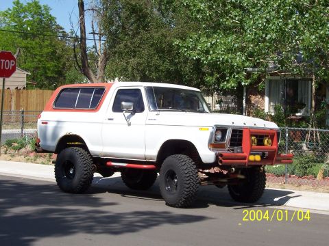 1978 Ford Bronco - A lifted 1978 Ford Bronco with a custom red bumper and orange roof sits on a street.