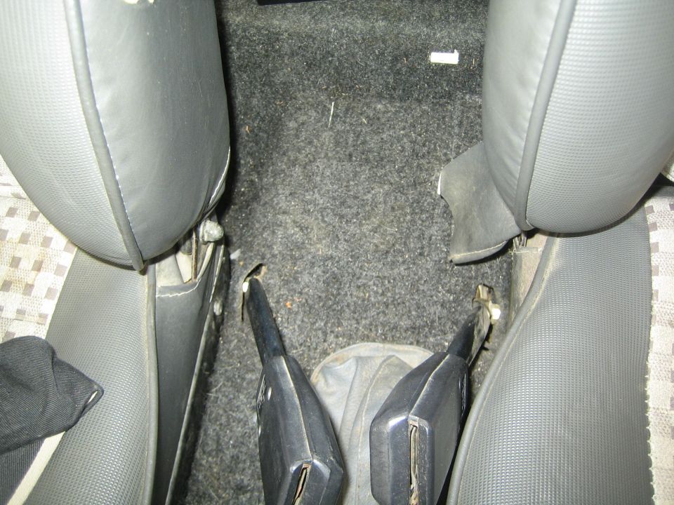 Car interior showing gray seats and black carpet with two seatbelt buckles visible