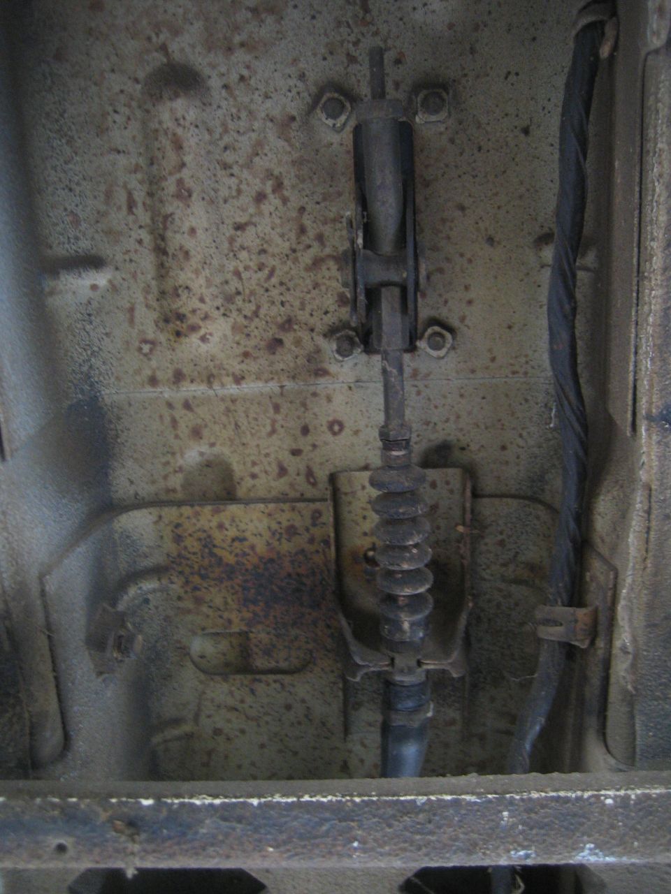 Underneath view of a vehicle's brake cable assembly, showing rust and a rubber boot