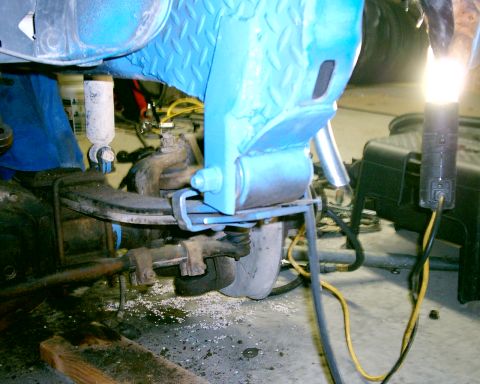 1985 Ford Bronco - Close-up of vehicle suspension components, showing a blue painted frame and a leaf spring.