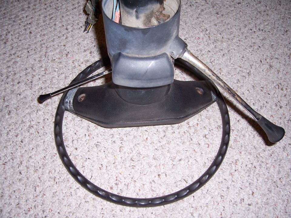 Black steering wheel and metal steering column with black plastic shroud and levers on a carpeted surface