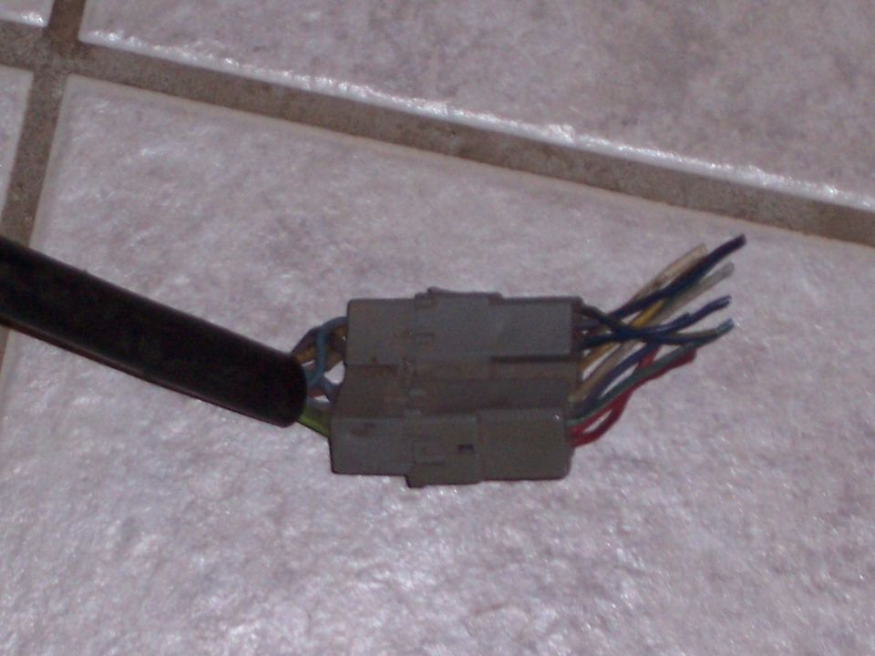 Close-up of a gray electrical connector with multiple colored wires coming out of a black cable. It's on a tiled floor