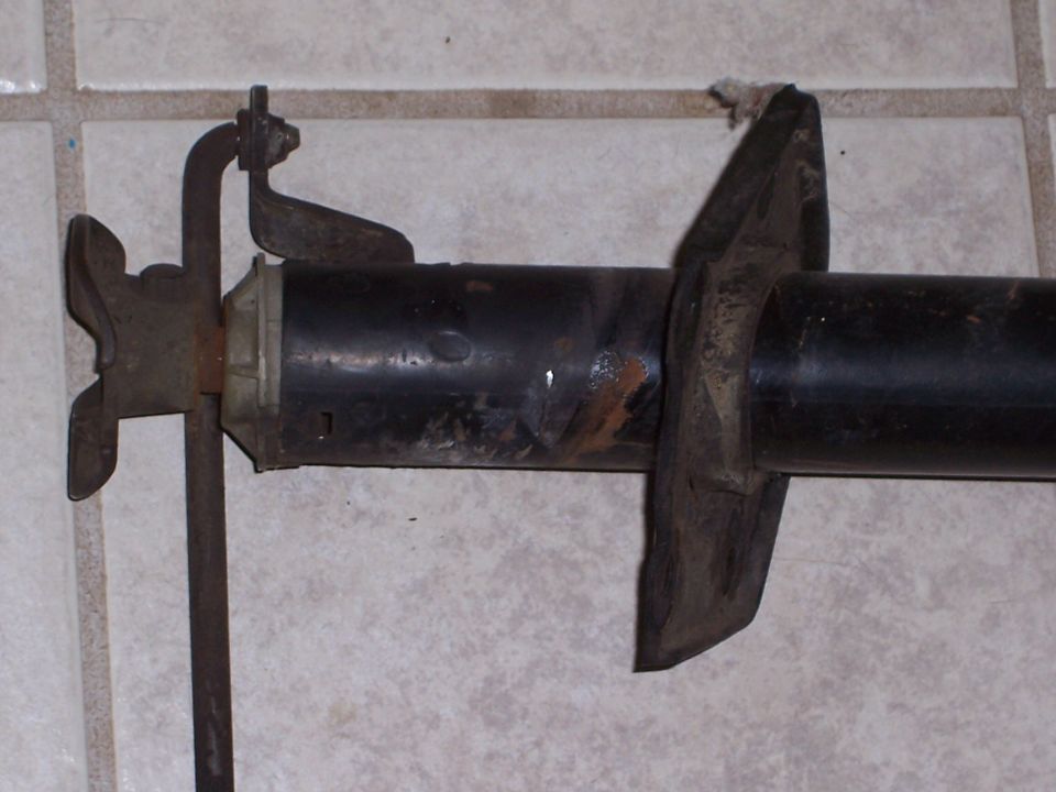 Rusty metal bracket attached to a black cylindrical automotive part