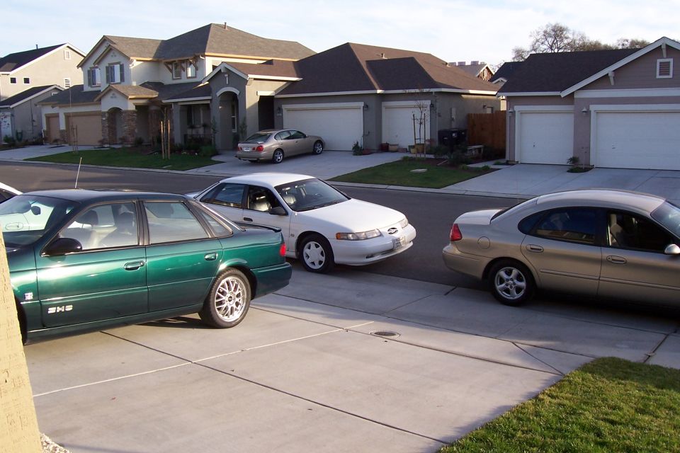 Green sedan, white sedan, and tan sedan parked in front of suburban houses