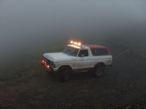 1978 Ford Bronco - A 1978 Ford Bronco is driven through a foggy, rocky terrain with its headlights and roof lights illuminated.