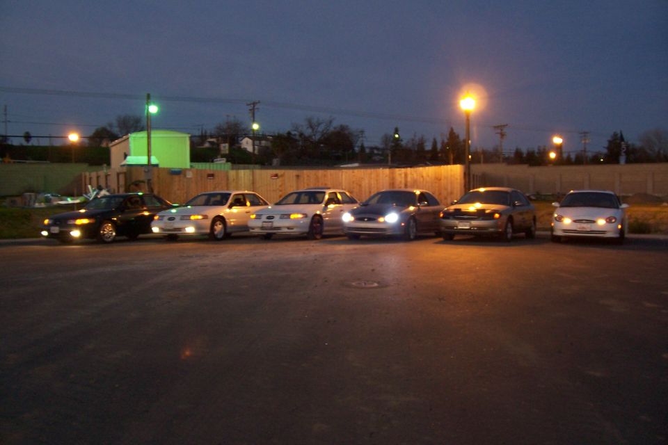Six sedans parked in a lot at dusk, including a 1998 Mercury Sable