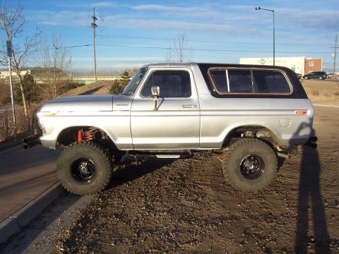 1978 Ford Bronco - This lifted 1978 Ford Bronco is shown from the side, parked on a dirt lot with a clear blue sky above.