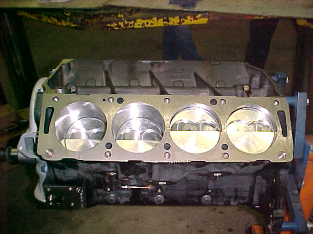 V8 engine short block with four polished pistons visible on deck, on a stand in a shop