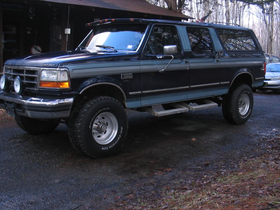 Black lifted four-door Ford crew cab truck conversion in a driveway