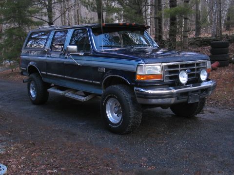 1979 Ford Bronco - This dark blue SUV, likely a Ford Centurion conversion, features prominent off-road tires and chrome accents, parked in a wooded area.