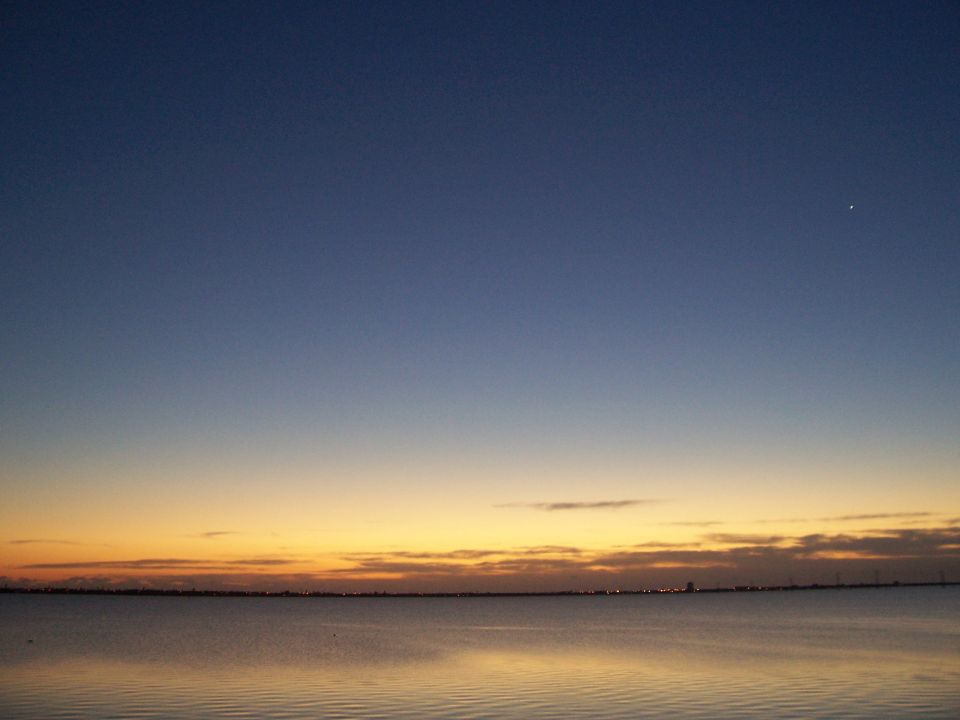 Water reflects sunset colors under a gradient sky with a distant city skyline