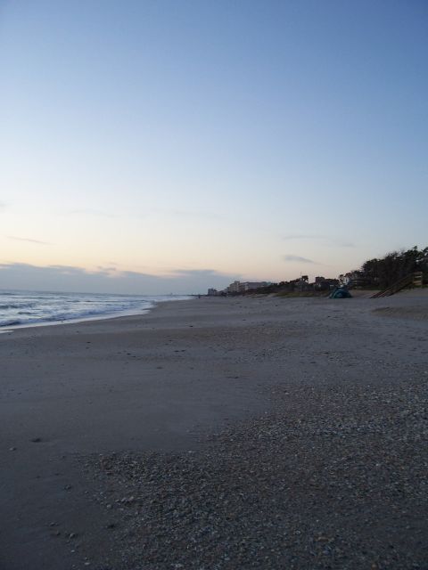 1994 Ford Probe - A beach scene unfolds with gentle waves lapping the shore and buildings visible in the distance under a pale blue sky.