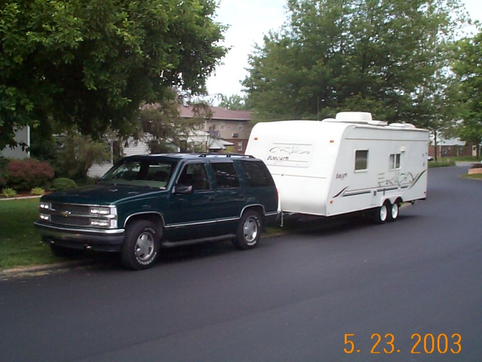 Green Chevy SUV hitched to a white Bobcat travel trailer parked on a residential street, dated 5.23.2003