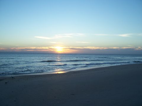 1994 Ford Probe - The sun rises over the ocean, casting light on the waves and sandy shore.