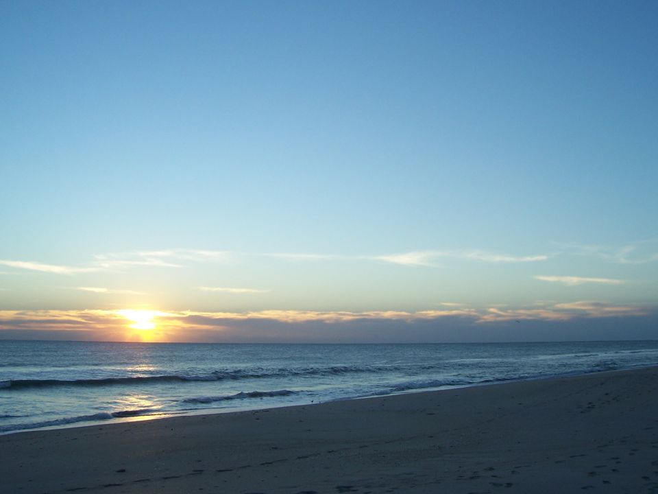Beach and ocean with sunset on the horizon. SUPERMOTORS.NET logo in lower right