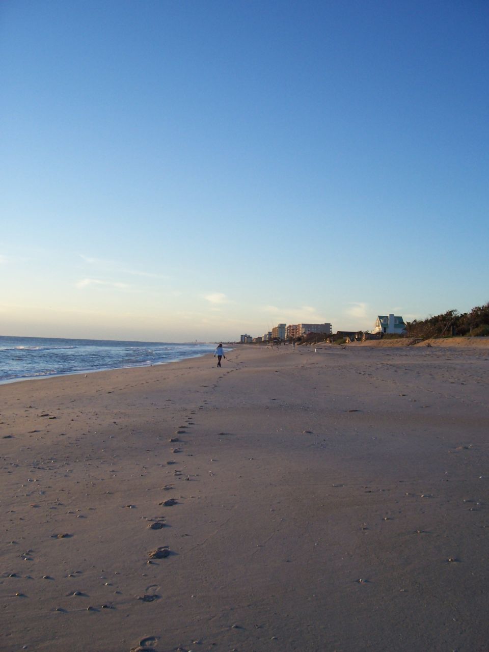 Beach scene with footprints in sand and a person walking near the ocean