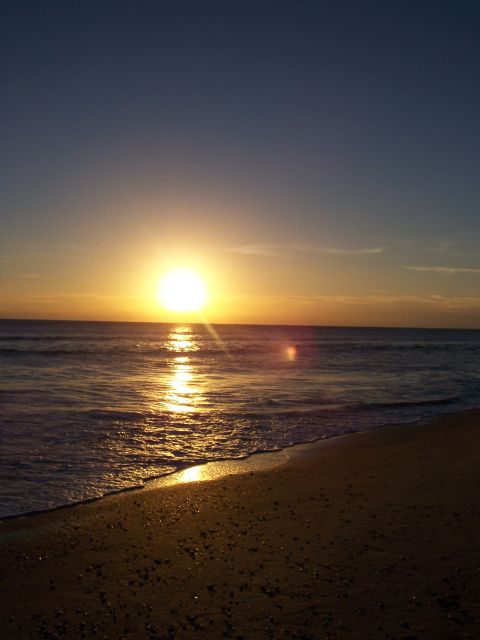1994 Ford Probe - The sun sets over the ocean, casting a golden reflection on the water and beach.