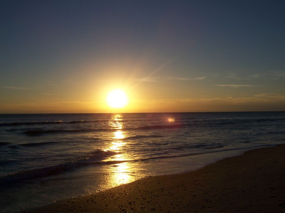 Sunset over the ocean with waves crashing on a sandy beach. Text overlay reads SUPERMOTORS