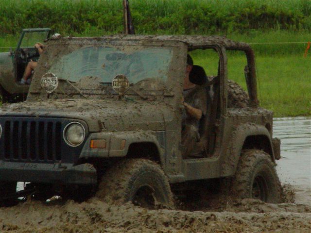Doorless Jeep Wrangler TJ covered in mud driving through a mud pit with Hella lights on the windshield