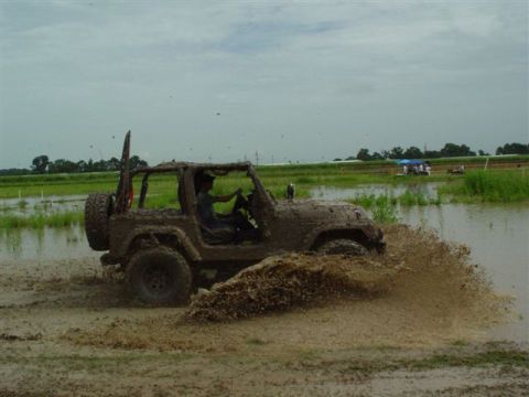 2002 Jeep Wrangler - A Jeep Wrangler navigates a muddy off-road course, kicking up a large spray of water and mud.