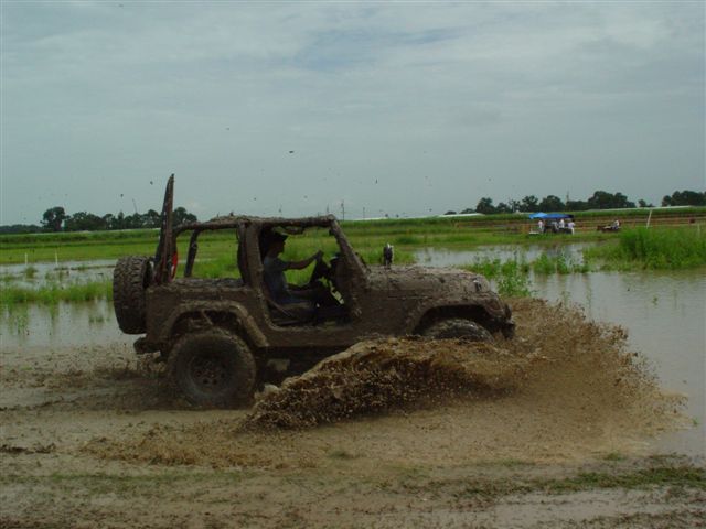 Mud-covered topless Jeep Wrangler splashing through a flooded muddy field