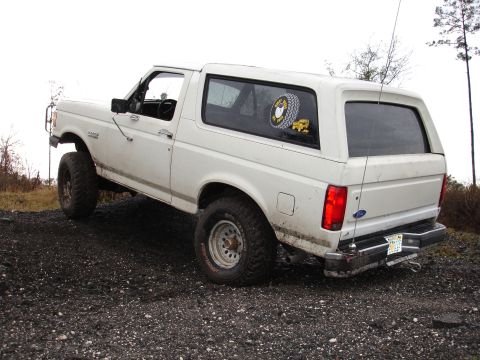 1989 Ford Bronco - This lifted Ford Bronco is parked on a gravel surface, showing its off-road modifications and a sticker on the rear window.