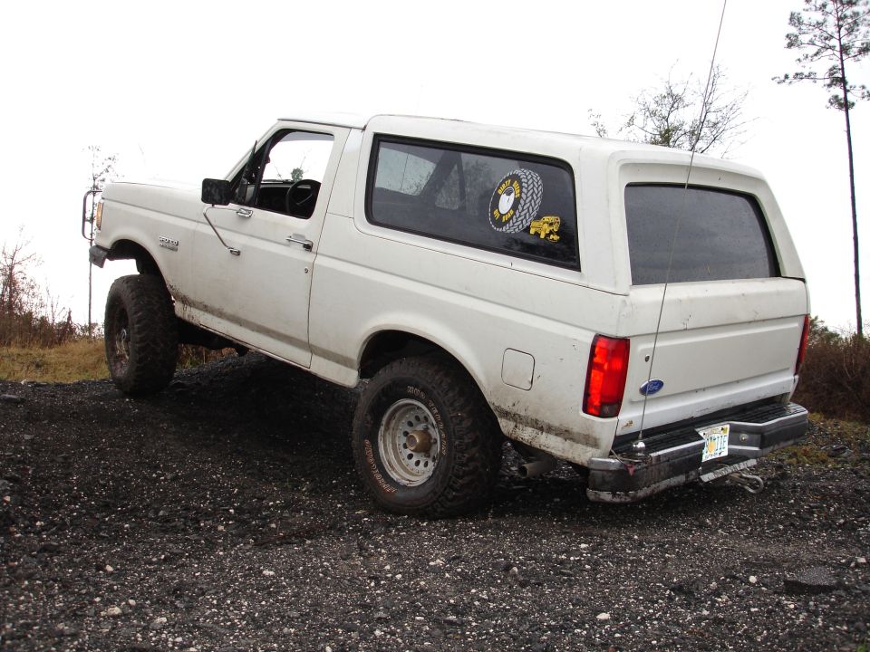 White Ford Bronco parked on gravel, lifted with off-road tires. Has a tire sticker on the rear window
