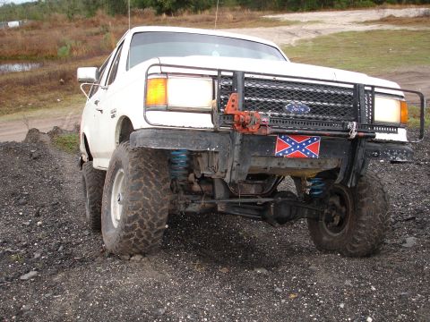 1989 Ford Bronco - This modified Ford Bronco sits on a gravelly surface, a prominent winch and a controversial flag on its front end.