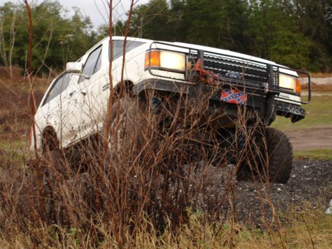 1989 Ford Bronco - A white Ford Bronco navigates rough terrain, its front end lifted high.