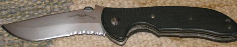 1984 Ford Bronco - A folding knife with a partially serrated blade and a black handle is shown against a textured background.