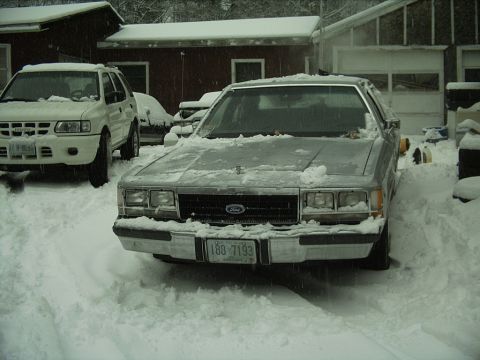 1991 Ford LTD Crown Victoria - A silver sedan sits covered in snow, with another white SUV visible to the left.