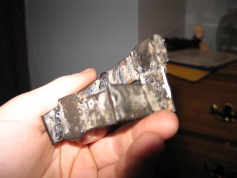 1995 Ford Bronco - A close-up view of a crudely welded metal bracket being held by a person's hand.