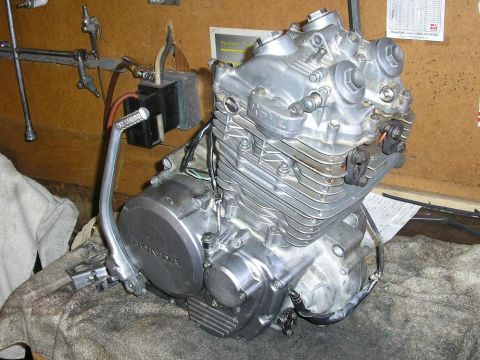 1900 Honda Big Red - A Honda motorcycle engine is shown on a workbench, with a kickstarter lever visible.