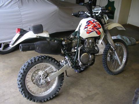 1900 Honda Big Red - This Honda dirt bike is parked indoors next to a covered vehicle.