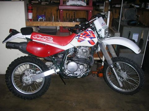 1900 Honda Big Red - A Honda dirt bike is parked in a workshop, showing its engine and suspension details.