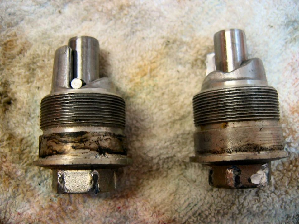 Two metal motorcycle carburetor parts with threaded sections and hex nuts at the bottom
