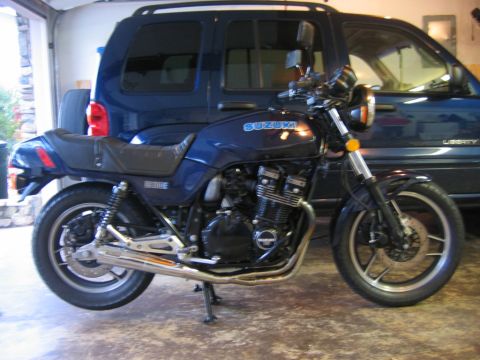 1985 Ford LTD Crown Victoria - A blue Suzuki motorcycle is parked in front of a dark blue SUV inside a garage.