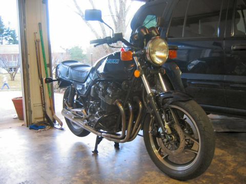 1985 Ford LTD Crown Victoria - A black Suzuki motorcycle is parked in a garage, with a dark SUV visible behind it.
