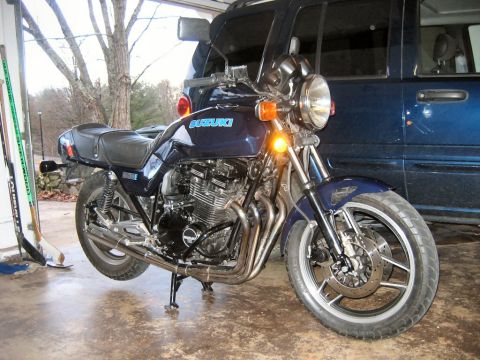 1985 Ford LTD Crown Victoria - A Suzuki motorcycle is parked in a garage, with a dark blue SUV behind it.