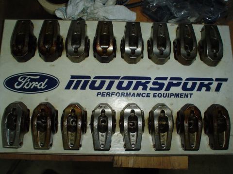 1984 Ford Bronco - Sixteen stamped-steel V8 rocker arms laid out in two rows of eight on a white Ford Motorsport Performance Equipment board, some showing bro…